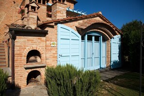 Un bâtiment traditionnel en briques, doté d’une entrée en arc de pierre, d’une porte bleue et d’un petit four en briques.