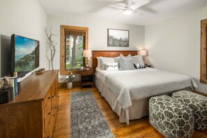 A bedroom with a bed, bedside tables, a desk, a chair, a rug, and a ceiling fan.