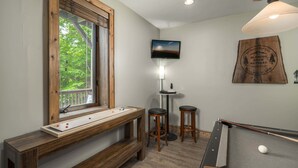 Una habitación con mesa de billar, mesa de juego de discos, televisor y ventana con vistas a árboles.