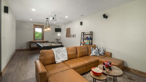 Una sala de estar con un sofá de cuero marrón, una mesa de billar y una mesa de futbolín.
