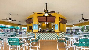 Un espace extérieur aménagé en terrasse, avec des tables et des chaises, un bar central et des ventilateurs de plafond.