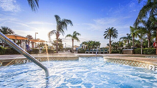 Une piscine dont la profondeur est indiquée à 2 pieds et 9 pouces, entourée de palmiers et de chaises longues.