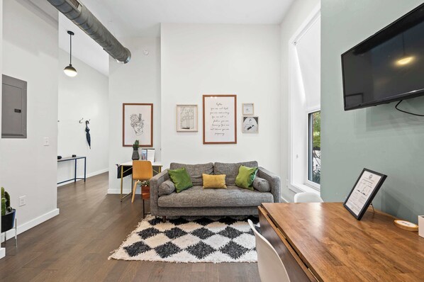 Ein modernes Wohnzimmer mit grauem Sofa, einem schwarz-weißen Teppich und gerahmten Kunstwerken an der Wand.