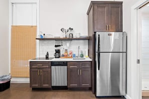A compact kitchen with dark wooden cabinets, a stainless steel refrigerator, and a white tiled backsplash.