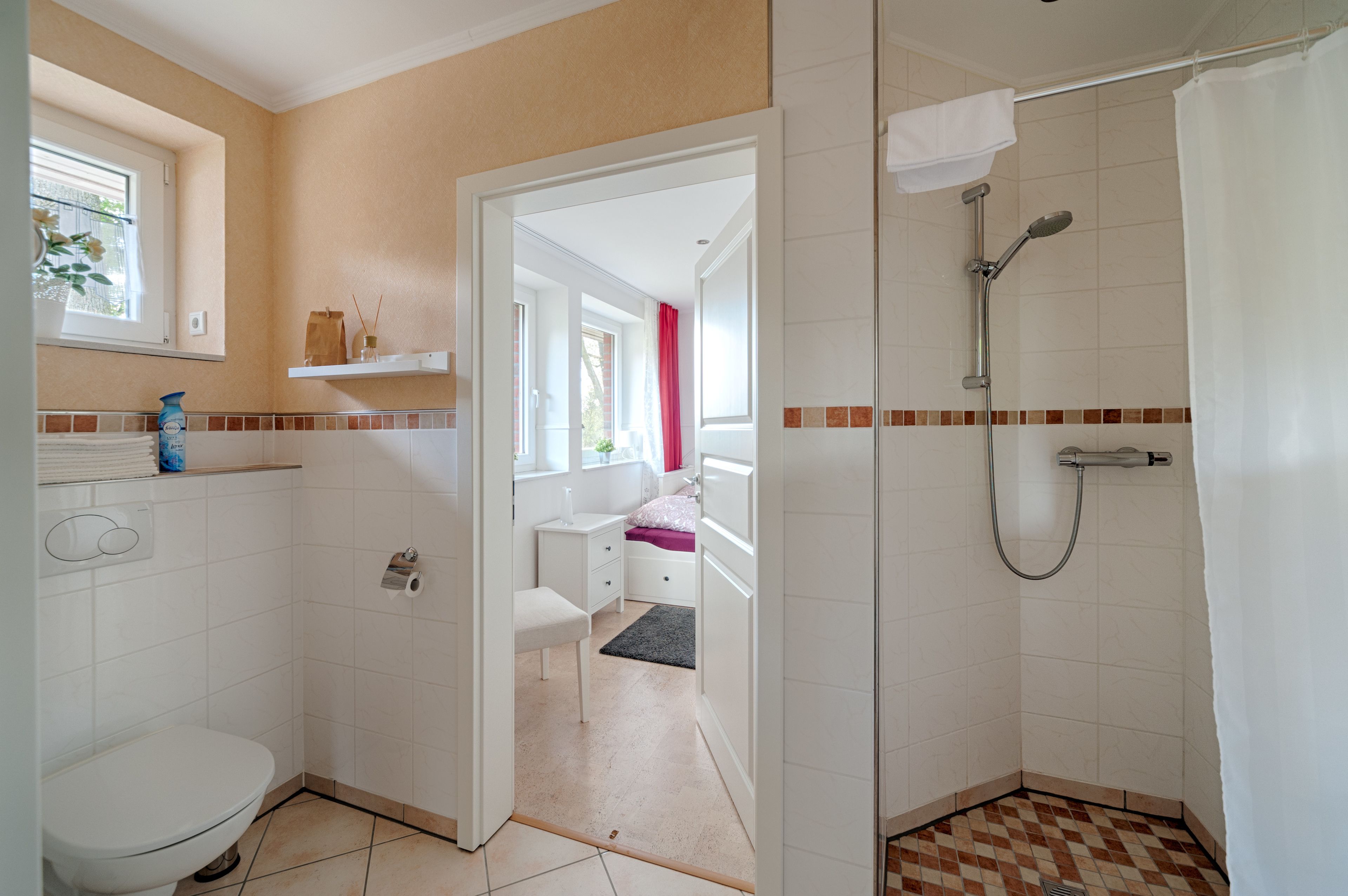 Een badkamer met toilet, douche en een klein nachtkastje met een roze kussen.