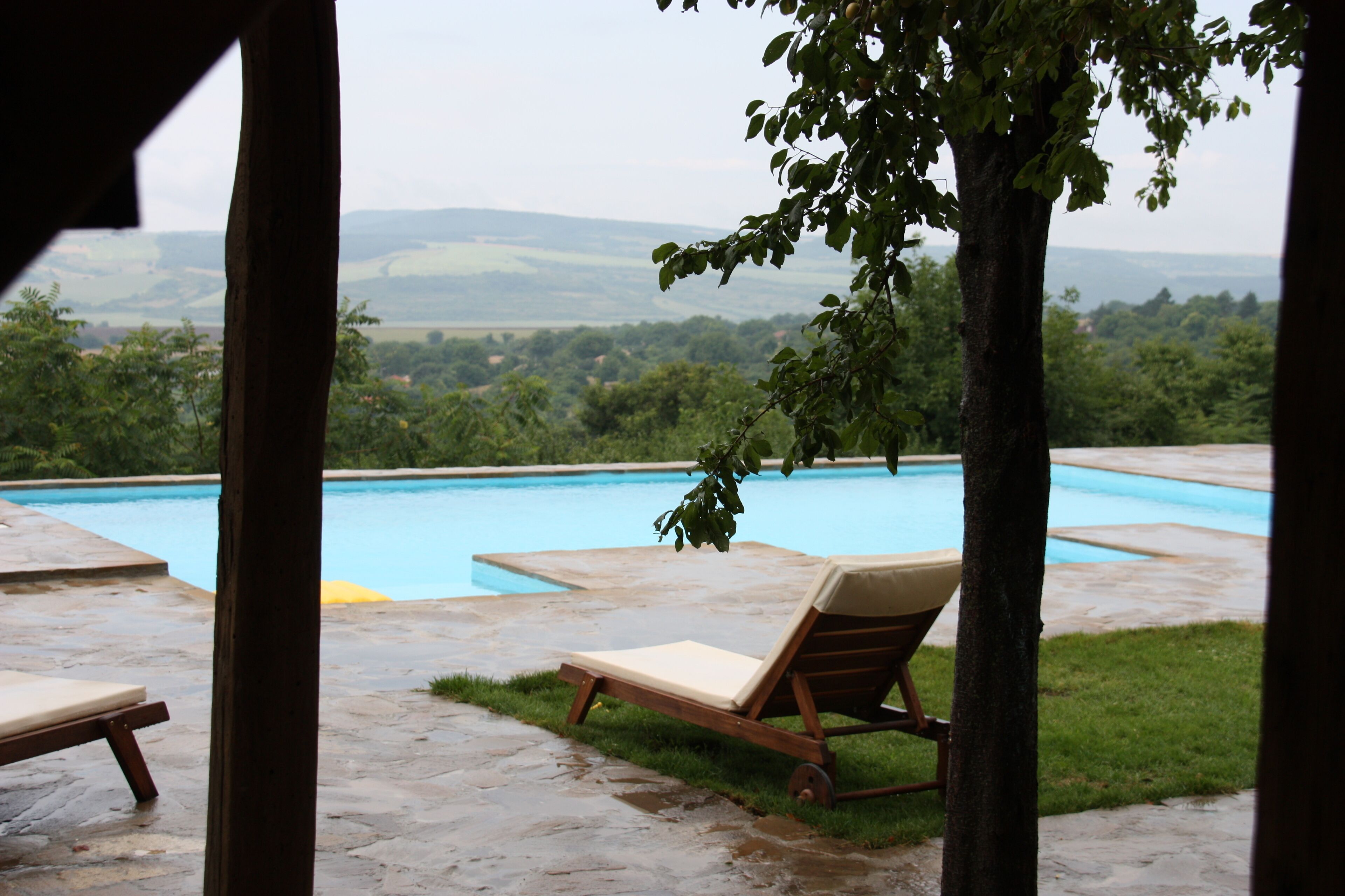 Une piscine entourée de chaises longues, bordée d’une terrasse en pierre et offrant une vue sur un paysage verdoyant.