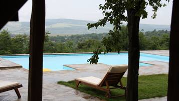 Une piscine entourée de chaises longues, bordée d’une terrasse en pierre et offrant une vue sur un paysage verdoyant.