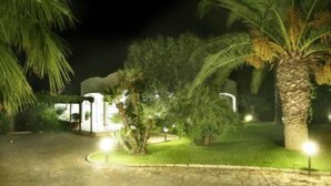 A nighttime view of a hotel entrance with a paved pathway, palm trees, and illuminated lights. - Magnificent sea view villa with large garden, a few steps from the sea (Gallipoli)
