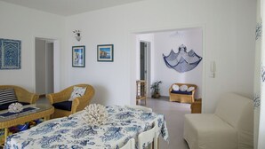 A spacious living room with a dining area, featuring wicker furniture, a chandelier, and wall art. - Magnificent sea view villa with large garden, a few steps from the sea (Gallipoli)
