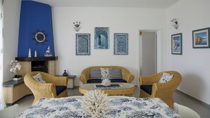 A living room with a blue accent wall, a fireplace, wicker furniture, and decorative wall art. - Magnificent sea view villa with large garden, a few steps from the sea (Gallipoli)