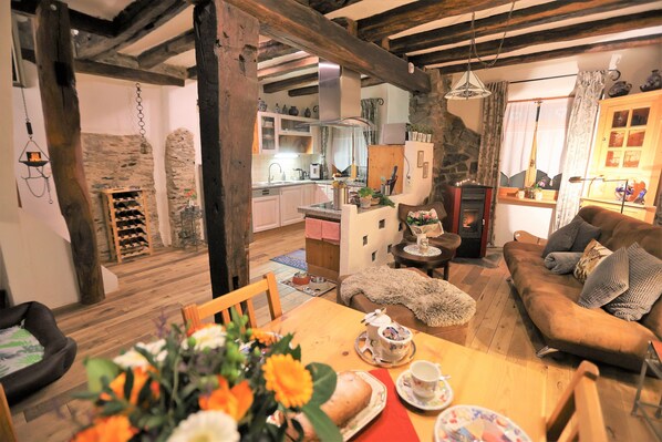A cozy living room with a wooden table set for tea, a sofa, and a kitchen in the background.