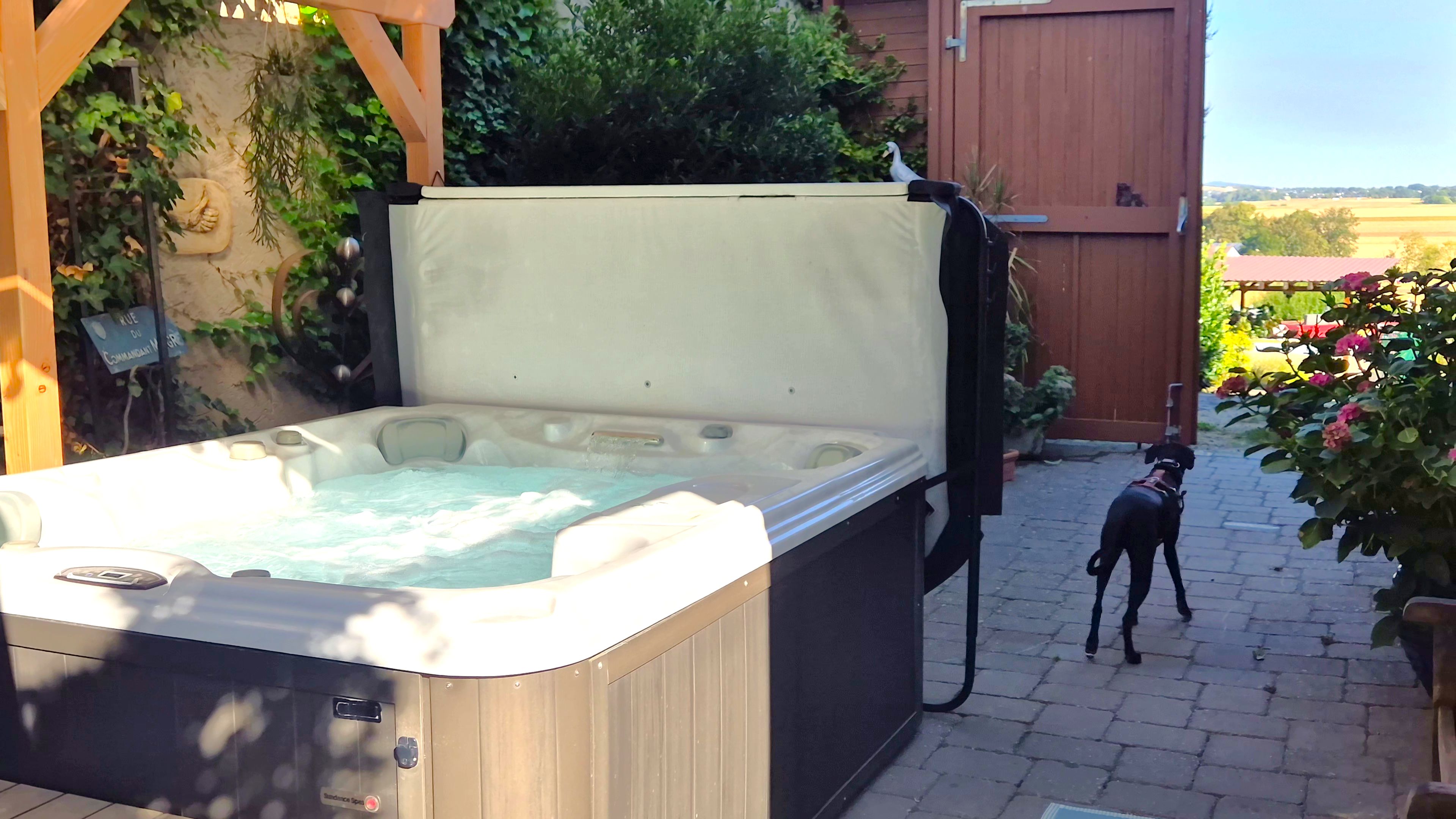 Een hottub met een houten deksel, omgeven door groen en een houten schutting.