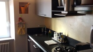 A compact kitchen with a gas stove, a sink, and a small countertop. There is a window providing natural light, and a radiator is visible on the left. - Apartament roccabella (Jesi)