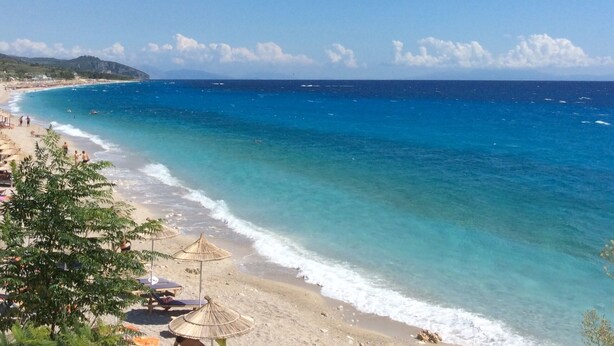 A beach with clear blue waters, a sandy shore, and a few umbrellas. - Apartament roccabella (Jesi)