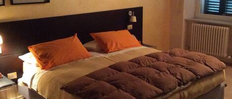 A bedroom with a bed, two pillows, a nightstand, a lamp, a framed picture, and a window with blinds.