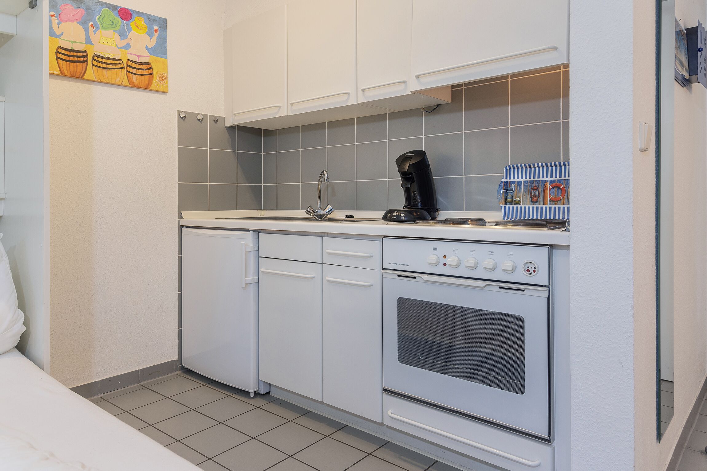 Eine kleine Küche mit weißen Schränken, einem Einbauofen und einer Kaffeemaschine.