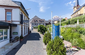 A cobblestone street leading to a hotel with a sign indicating it is a hotel. There are buildings with traditional architecture and a church in the background. - Hotel Winzerverein (Zeltingen-Rachtig)