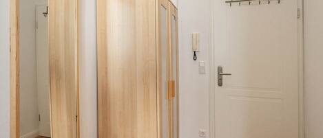 A room with a wooden wardrobe, a white door with a coat hook, and a telephone on the wall.