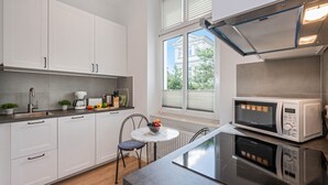 A modern kitchen with white cabinets, a built-in microwave, a stove, and a small dining area with a table and chairs. - Cozy vacation apartment in Heringsdorf close to the beach (Seebad Heringsdorf)