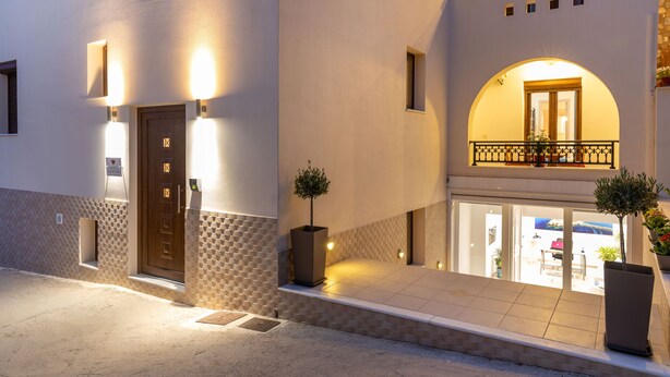 A modern building with a well-lit entrance, a balcony with a railing, and a door with a small window. - Naxos Diamond Studios Apartments (Naxos)