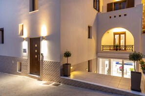 A modern building with a well-lit entrance, a balcony with a railing, and a door with a small window. - Naxos Diamond Studios Apartments (Naxos)