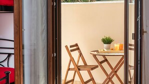 An open sliding door leading to a balcony with a table, chairs, a potted plant, and two glasses of orange juice. - Naxos Diamond Studios Apartments (Naxos)