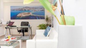 A modern office space with a glass desk, a white sofa, and a large scenic painting of a coastal landscape. - Naxos Diamond Studios Apartments (Naxos)