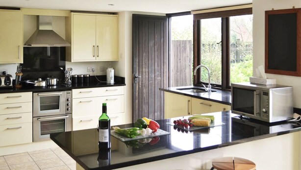 A modern kitchen with stainless steel appliances, a large island with fresh produce, and a view of the outdoors through a window.