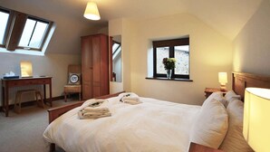 A bedroom with a large bed, a desk, a chair, a wardrobe, and a window with a view.