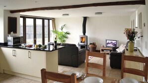 A kitchen with a built-in stove, a dining area with chairs and a table set for two, and a living area with a sofa and a television.