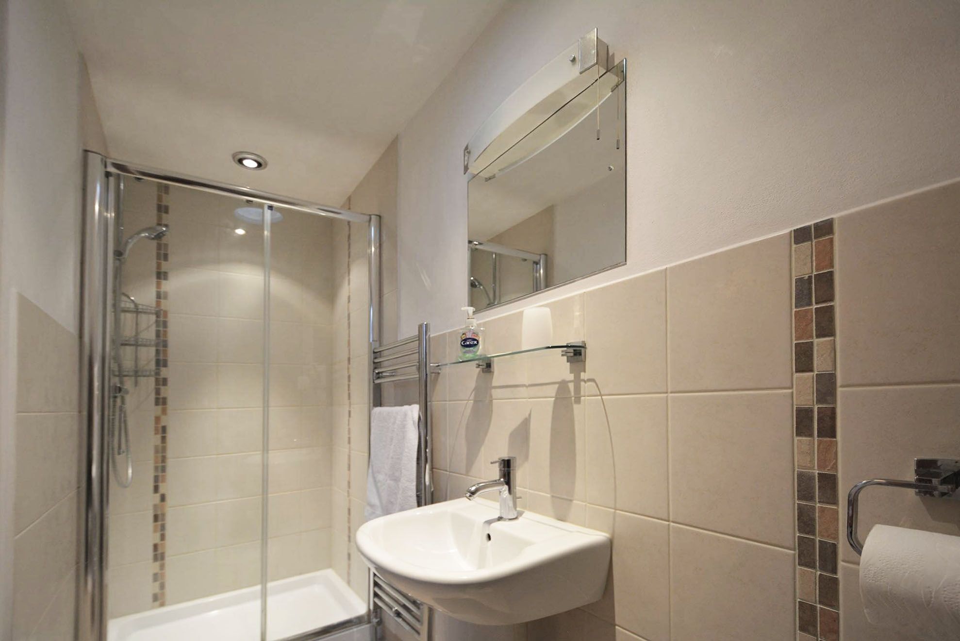 Un baño moderno con ducha envuelta en vidrio, lavamanos blanco y espejo sobre el lavamanos.