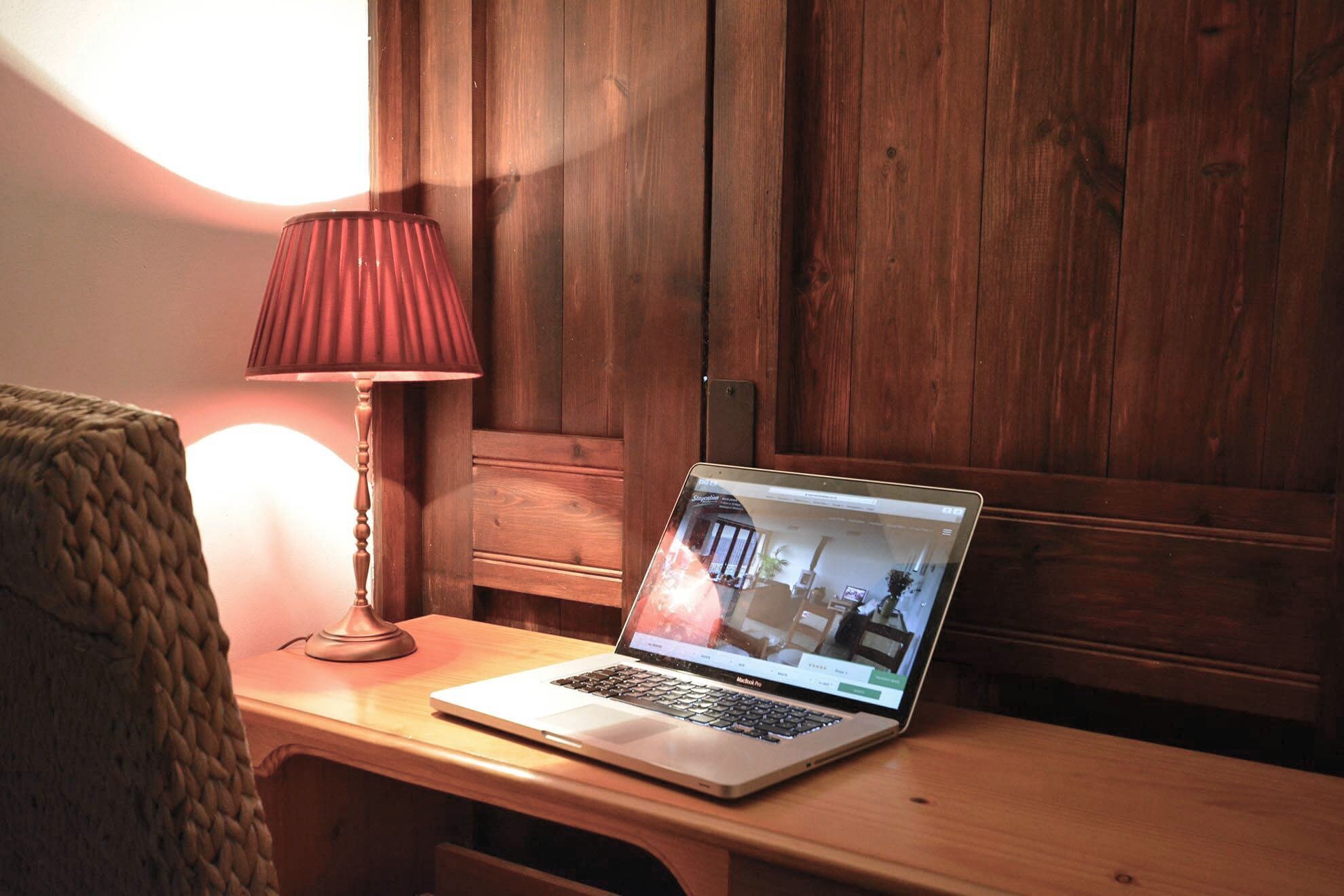 Een laptop op een houten bureau met een lamp, voor een houten wand.