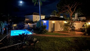 A nighttime view of a residential area with a swimming pool, palm trees, and houses with lit windows. - Andalusian villa, pool 4x8m, 2 double beds, beach 400M, close to restaurants (Las Chapas)