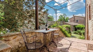 Une terrasse extérieure avec un mur en pierre, deux chaises en métal, une table et une structure en forme de pergola.