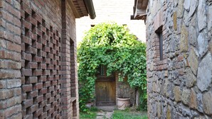Une ruelle étroite, bordée d’un mur de briques à gauche et d’un mur de pierres à droite, qui mène à une porte en bois surmontée d ’un arc orné de lierre.