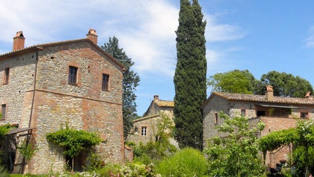 Un bâtiment en pierre doté d’une petite fenêtre et d’une cheminée, entouré de verdure et d’arbres.
