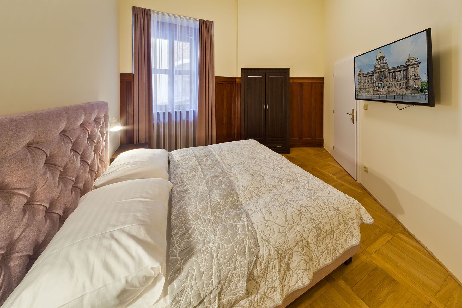 A bedroom with a bed, a wardrobe, a painting, and a window with curtains.