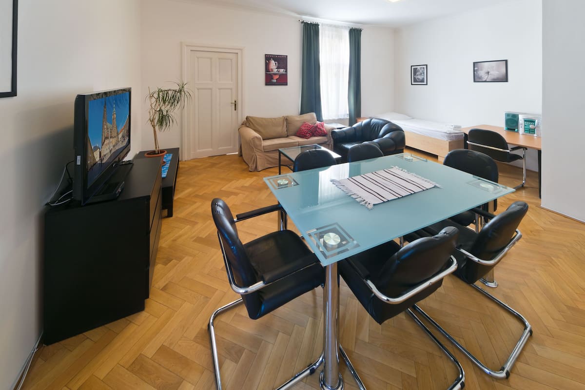 A modern living room with a glass dining table, black leather chairs, a beige sofa, and a television on a stand.