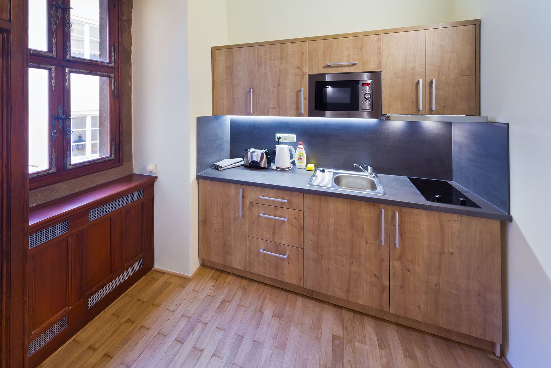 A compact kitchen with wooden cabinets, a built-in microwave, a sink, and a window with a view.