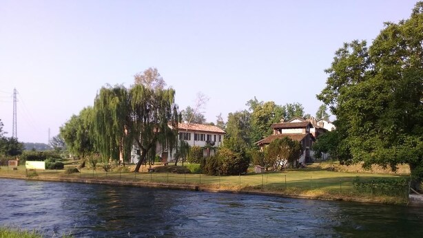 Ein Fluss mit Häusern am gegenüberliegenden Ufer, einer grünen Wiese und Bäumen.