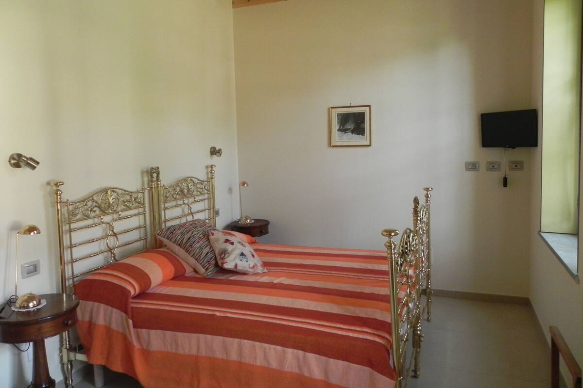 Une chambre à coucher avec un lit, des tables de chevet, une télévision et une fenêtre.