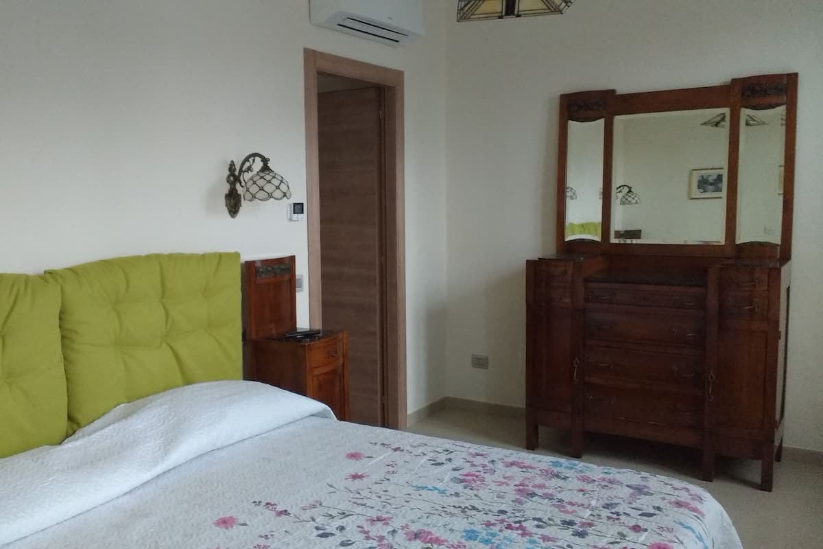 Une chambre à coucher avec un lit, une commode en bois, un miroir et une porte.