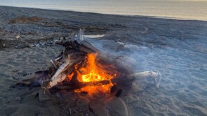 A beach scene with a campfire, sand, and a distant view of mountains. - Perfectly Positioned to Play on the Kenai Peninsula (Ninilchik)