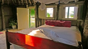A single bed with a red headboard in a room with a wooden ceiling and walls, a window with a view of the beach, and a potted plant. - Traditional Bure by the beach in the authentic Yasawa Village (Yasawa islands)