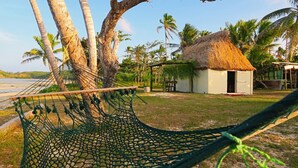 A hammock tied between palm trees, a thatched-roof hut, and a beach. - Traditional Bure by the beach in the authentic Yasawa Village (Yasawa islands)