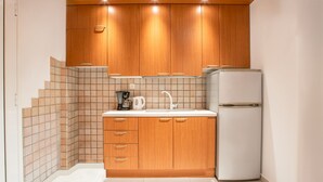 Eine kleine Küche mit Holzschränken, einer weißen Arbeitsplatte, einem Spülbecken, einer Kaffeemaschine und einem Kühlschrank.