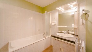 A bathroom with a bathtub, sink, and mirror. - Hotel Le Commerce (Dompaire)