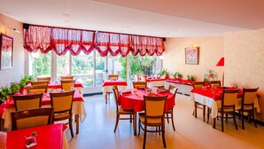 A restaurant with tables covered in red tablecloths, wooden chairs, and large windows with red curtains. - Hotel Le Commerce (Dompaire)