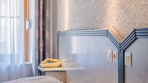 A hotel room with a bed, a bedside table, a mirror, and a textured wall. - Hotel Le Commerce (Dompaire)