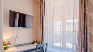 A small room with a desk, chair, TV, and window with curtains. - Hotel Le Commerce (Dompaire)